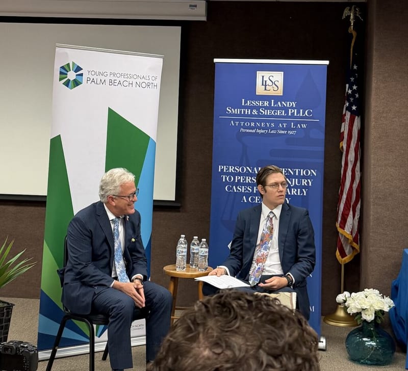John W. Brandes speaking at a Young Professionals of Palm Beach North ambassador event, seated alongside a moderator in front of a Lesser Landy Smith and Siegel PLLC sponsor banner