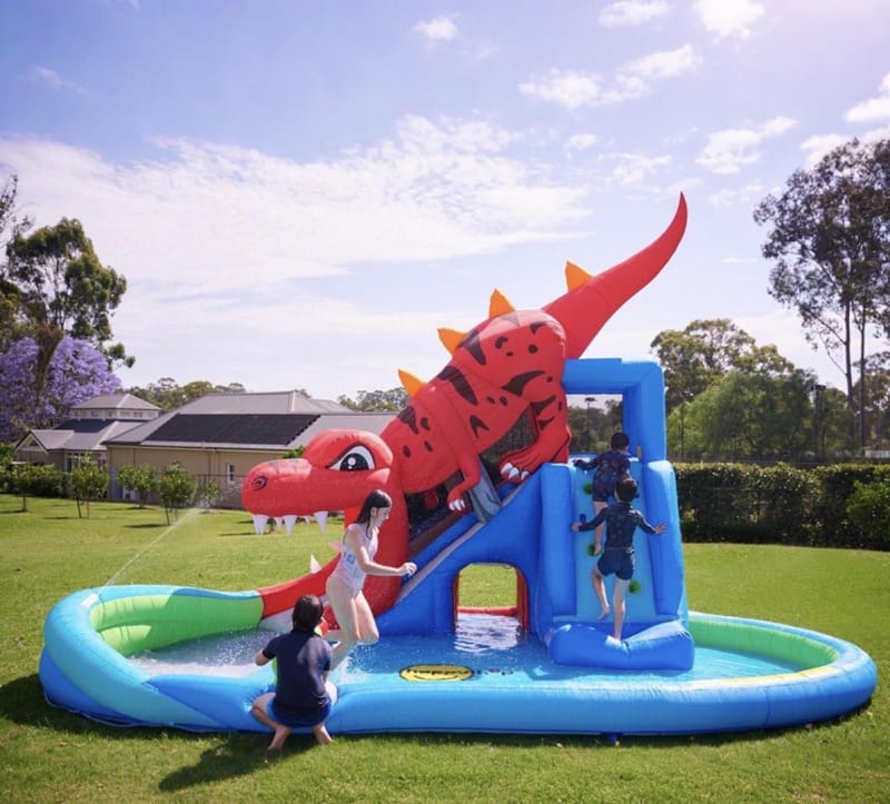 Kids playing on a red dragon water slide in the backyard